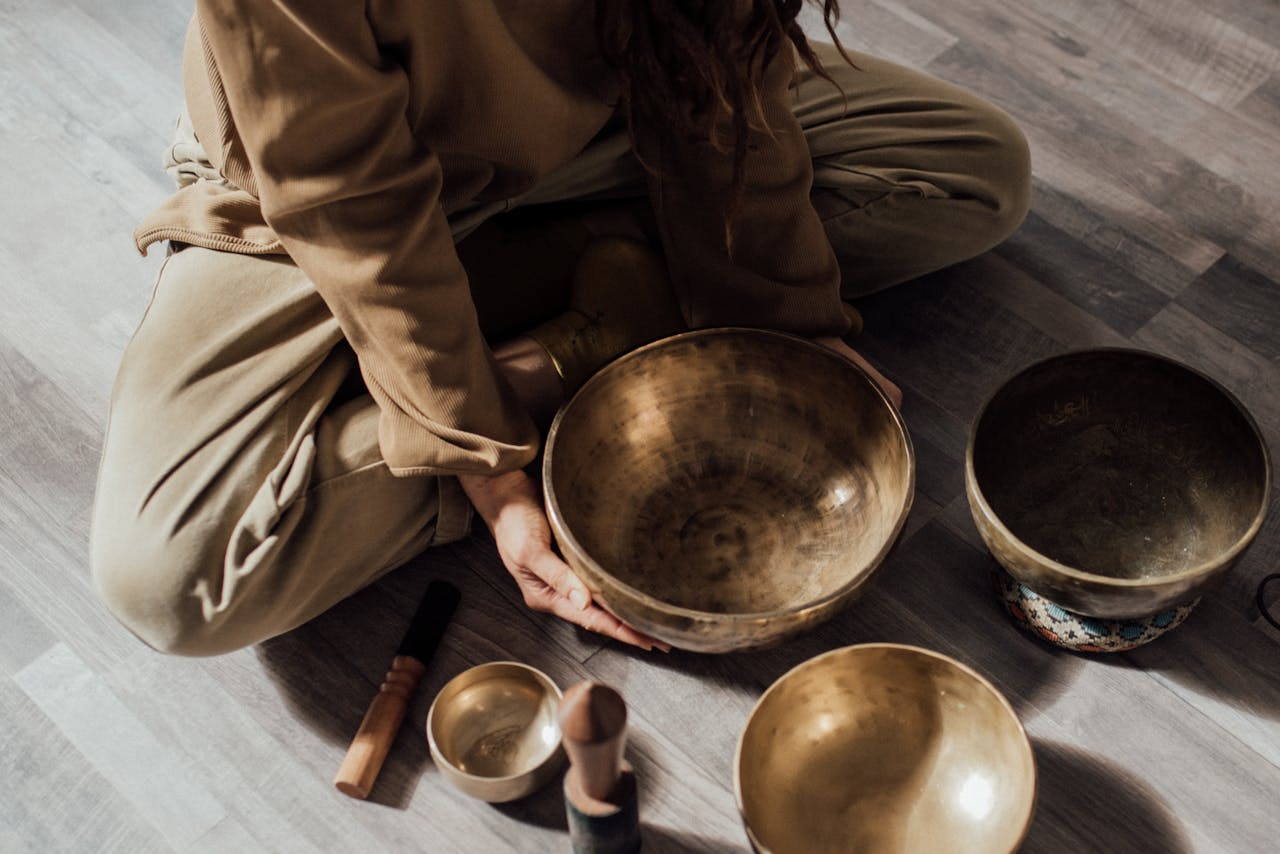 A person meditates with Tibetan singing bowls on a wooden floor, creating a serene atmosphere.